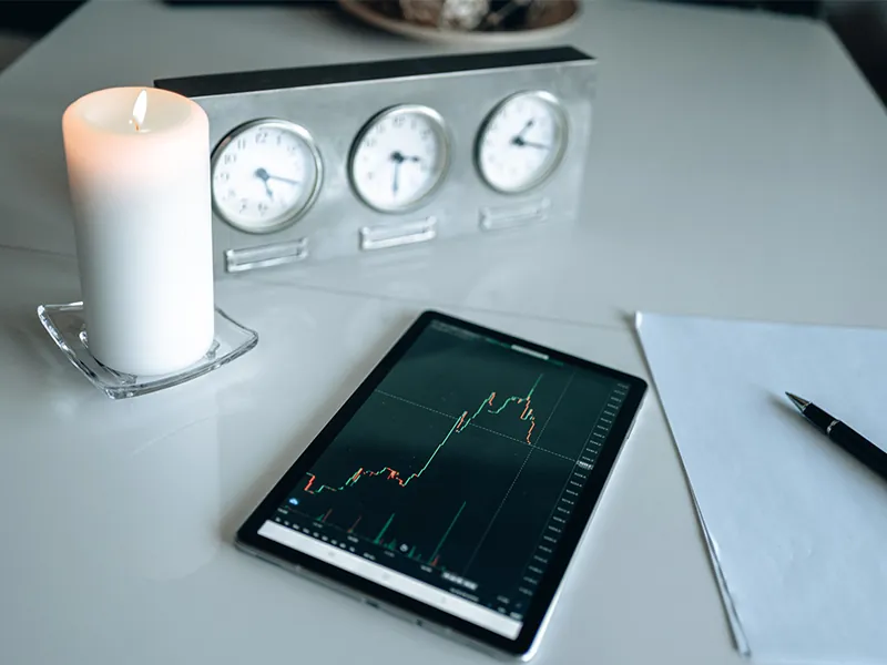 Tablet displaying a financial chart beside clocks, a notebook, and a candle.