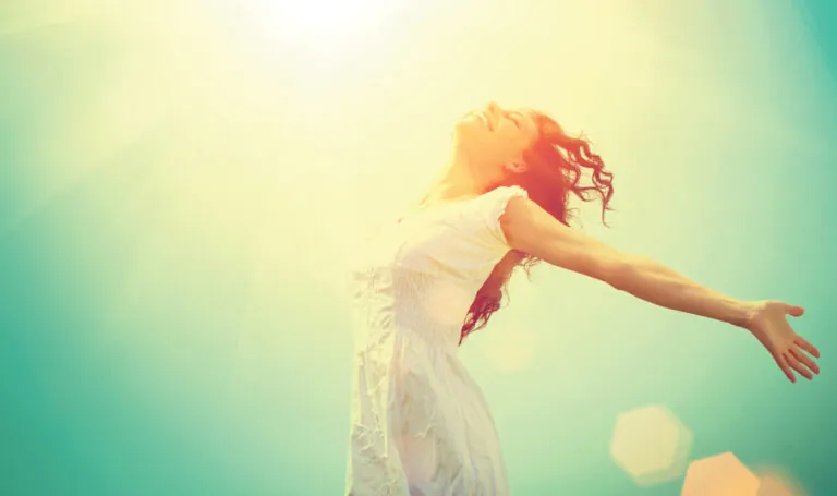 Woman standing outdoors with her arms outstretched toward the sunlight.