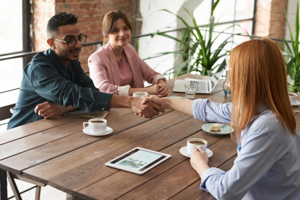 Three people meeting around a table, with two shaking hands.