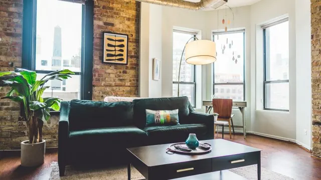 Apartment living room with a dark sofa, exposed brick walls, and large windows.