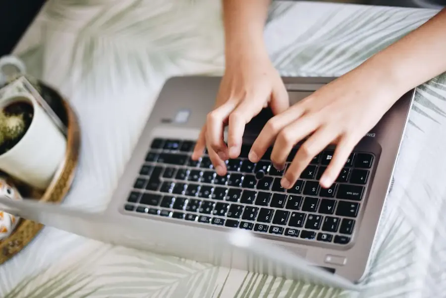 Person typing on a laptop beside a cup of coffee.