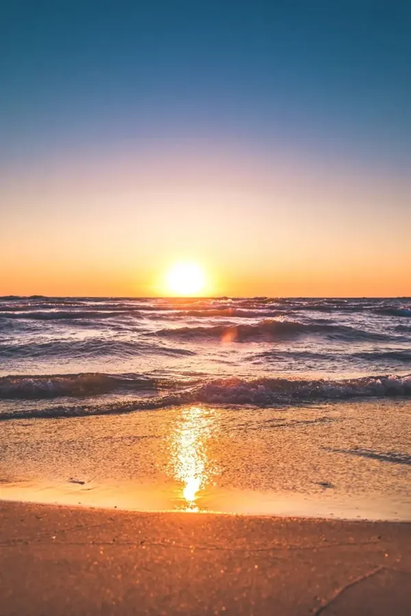 Sunset over the ocean with sunlight reflected on the wet sand.