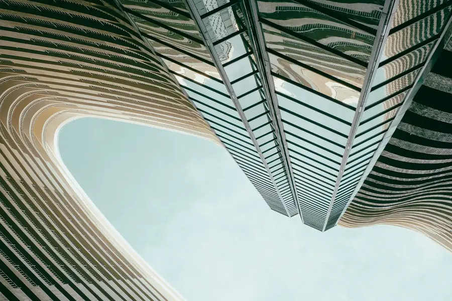 dba-why-dba-banner.webp Upward view between modern buildings with curved balconies.