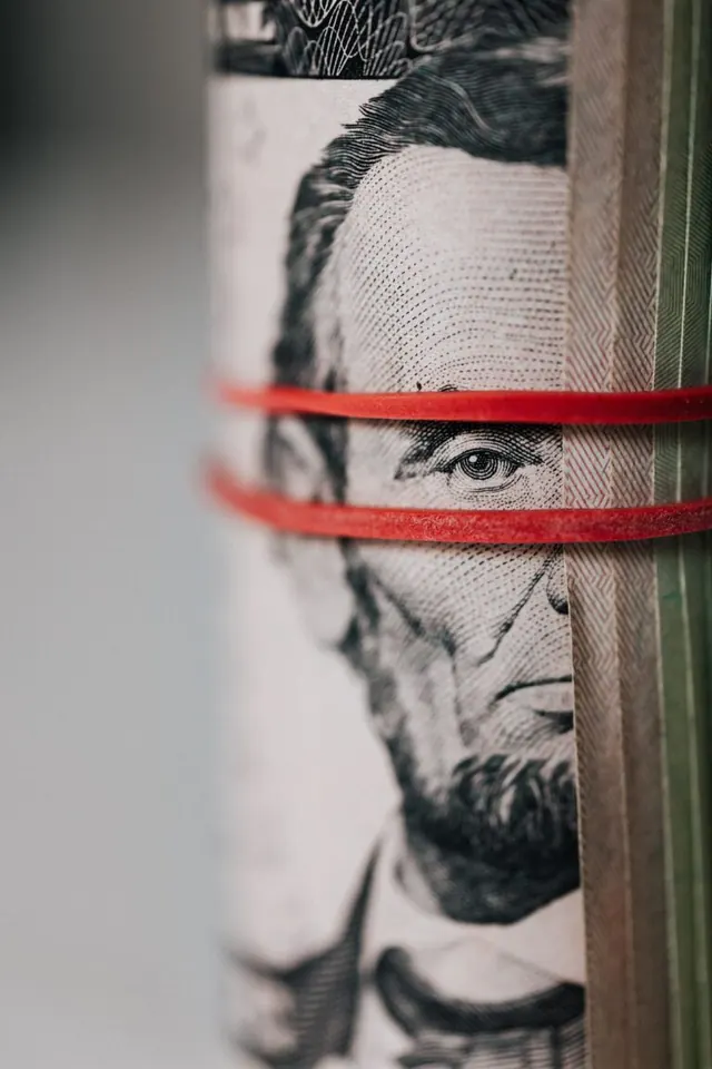 Rolled US dollar bills secured with red rubber bands.
