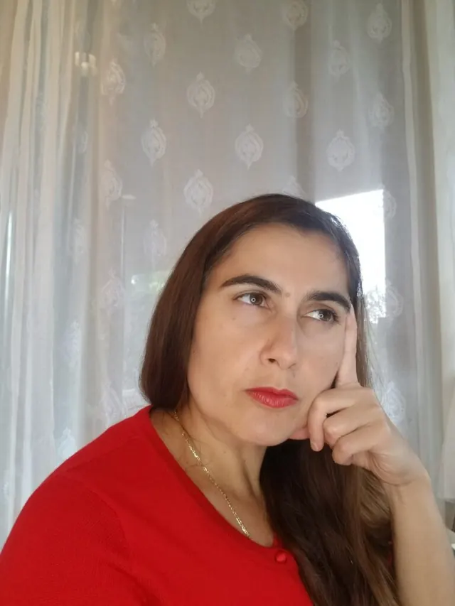 Woman in a red top resting her hand against her cheek in thought.