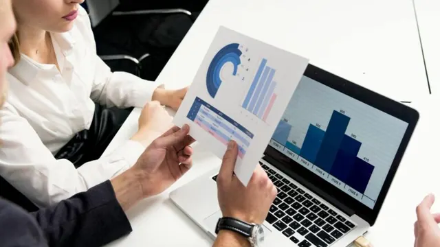 Professionals comparing printed financial charts with data on a laptop.